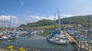 Ein Yachthafen mit mehreren angedockten Booten, im Hintergrund eine Brücke und eine hügelige Landschaft.