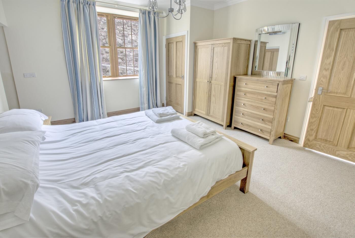 A bedroom with a large bed, wooden wardrobe, and a mirror.