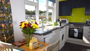 A modern kitchen with a view of the town, a washing machine, a microwave, and a dining area with a table and chairs. - 2 Bed in Teignmouth (oc-bchyvi) (Teignmouth)