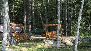 Un campamento con dos columpios de madera, un coche y una tienda de campaña en un área boscosa.