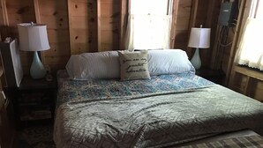 Un dormitorio acogedor con cama, almohadas, una mesita de noche y una lámpara.
