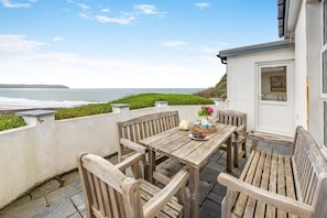 A wooden table and chairs on a patio with a view of the ocean. - 5 Bed in Mortehoe (oc-haro10) (Mortehoe)