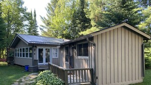 A small, single-story cabin with a porch and a separate shed.