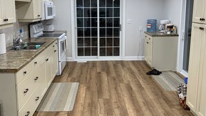 A spacious kitchen with wooden flooring, white cabinets, a microwave, and a large sliding glass door leading to a dining area.
