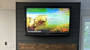 A flat-screen TV mounted on a wall above a fireplace, with a wooden shelf below.