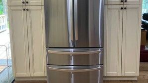 A stainless steel refrigerator in a kitchen with wooden cabinets and a wooden floor.