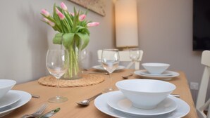 A dining table set with white plates, bowls, and cutlery, a vase with pink tulips, and a tall lamp. - 2 Bed in Braunton (oc-stabb) (Braunton)