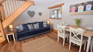 A cozy living area with a dark blue sofa, white chairs, a wooden dining table, and a staircase. - 2 Bed in Braunton (oc-stabb) (Braunton)