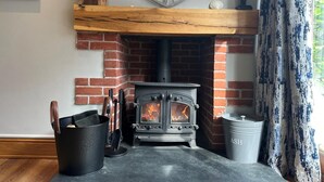 A wood-burning stove with a brick fireplace, a clock above it, and a bucket of ash beside it. - 2 Bed in Braunton (oc-stabb) (Braunton)