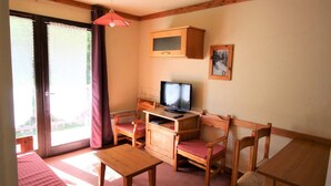 Een knus ingerichte kamer met een houten bureau, een televisie en een stoel. Er is een glazen schuifdeur naar een buitenruimte.