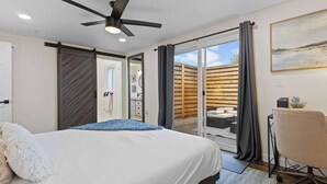 Een slaapkamer met een bed, een plafondventilator, een bureau en uitzicht op buiten.