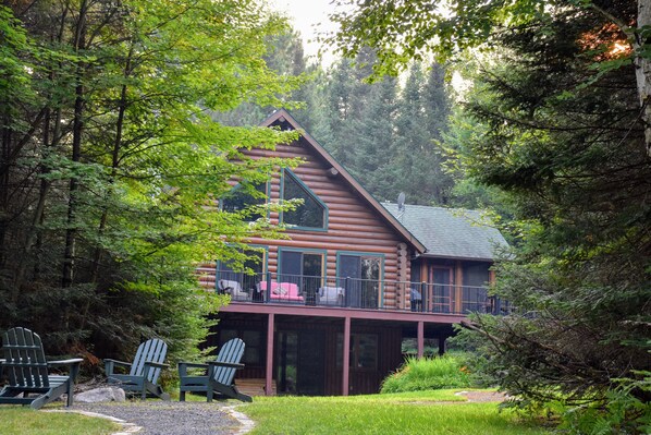 A log cabin with a balcony, surrounded by lush greenery.