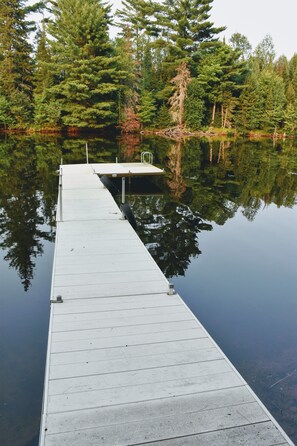 A wooden dock extending into calm water, surrounded by dense forest.