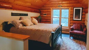 Ein Schlafzimmer in einer Blockhütte mit einem Bett, einem Sessel, einem Fenster und einem Deckenventilator.
