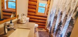 A bathroom with a wooden log wall, a sink with a soap dispenser, a toilet, and a window.