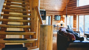 Ein Blockhaushaus-Interieur mit einer Holztreppe, einem Wohnbereich mit einer Couch und einem an der Wand befestigten Fernseher.