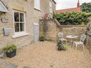 A stone cottage with a gravel patio, white outdoor furniture, and potted plants. - Snowdrop Cottage (Scarborough)