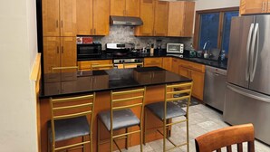 Une cuisine moderne avec des meubles en bois, un îlot central doté de tabourets de bar, des appareils électroménagers en acier inoxydable et une fenêtre donnant sur la ville.
