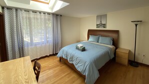 Une chambre avec une lucarne, un lit avec une literie bleue, une table de chevet en bois, une lampe sur pied et un tableau représentant la Tour Eiffel.