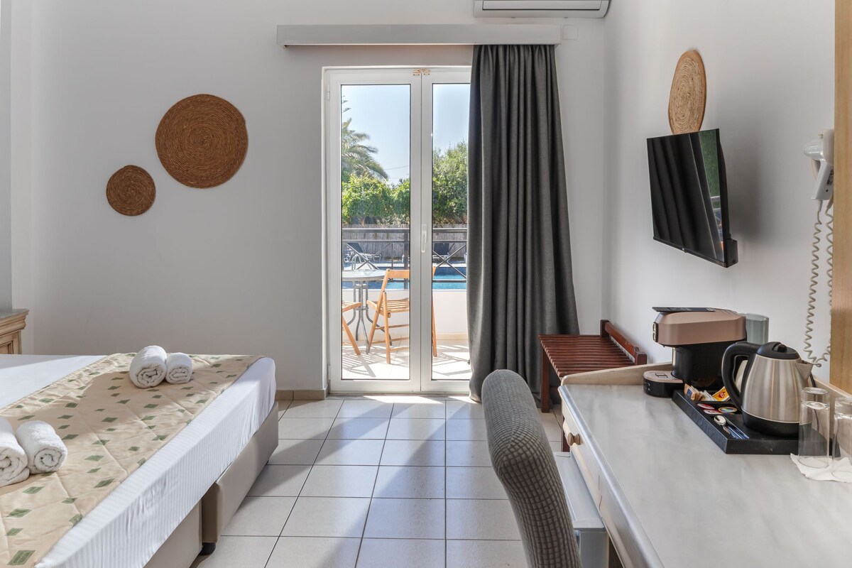 Une chambre d’hôtel comprenant un lit, un bureau avec une machine à café, une télévision et une vue sur une piscine et du mobilier d’extérieur.