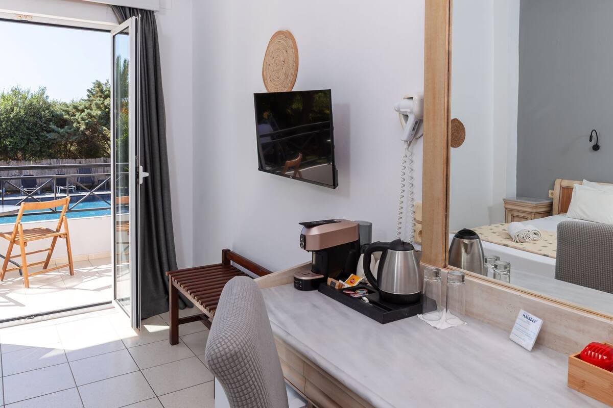 Habitación de hotel con balcón, cafetera, hervidor de agua, mesita de noche y un espejo grande.