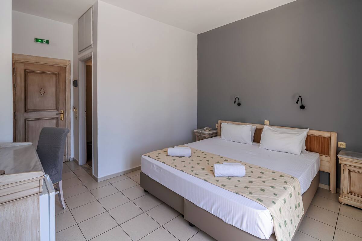Una habitación de hotel con una cama, una silla, un escritorio, una mesita de noche y una puerta.
