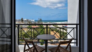 Un balcon avec une table et des chaises, offrant une vue sur la côte, avec des bâtiments et des arbres.