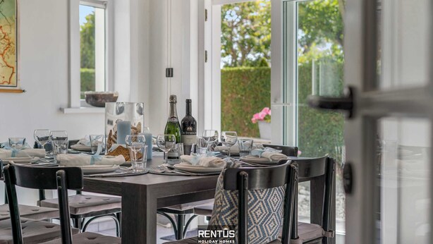 Un comedor con una mesa dispuesta para seis, un mapa en la pared y vistas a zonas verdes al exterior.
