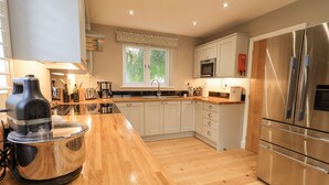 A modern kitchen with wooden countertops, stainless steel appliances, and a window with a view of greenery.