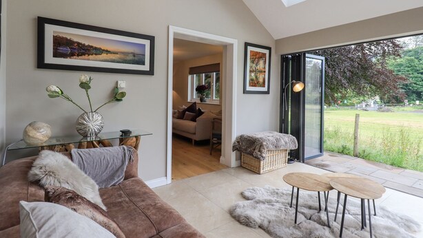 A modern living room with a brown sofa, a glass coffee table, and a fur rug. There is a painting on the wall and a window with a view of the outdoors.