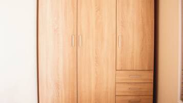 A room with a wooden wardrobe, a small table, and two cushions.