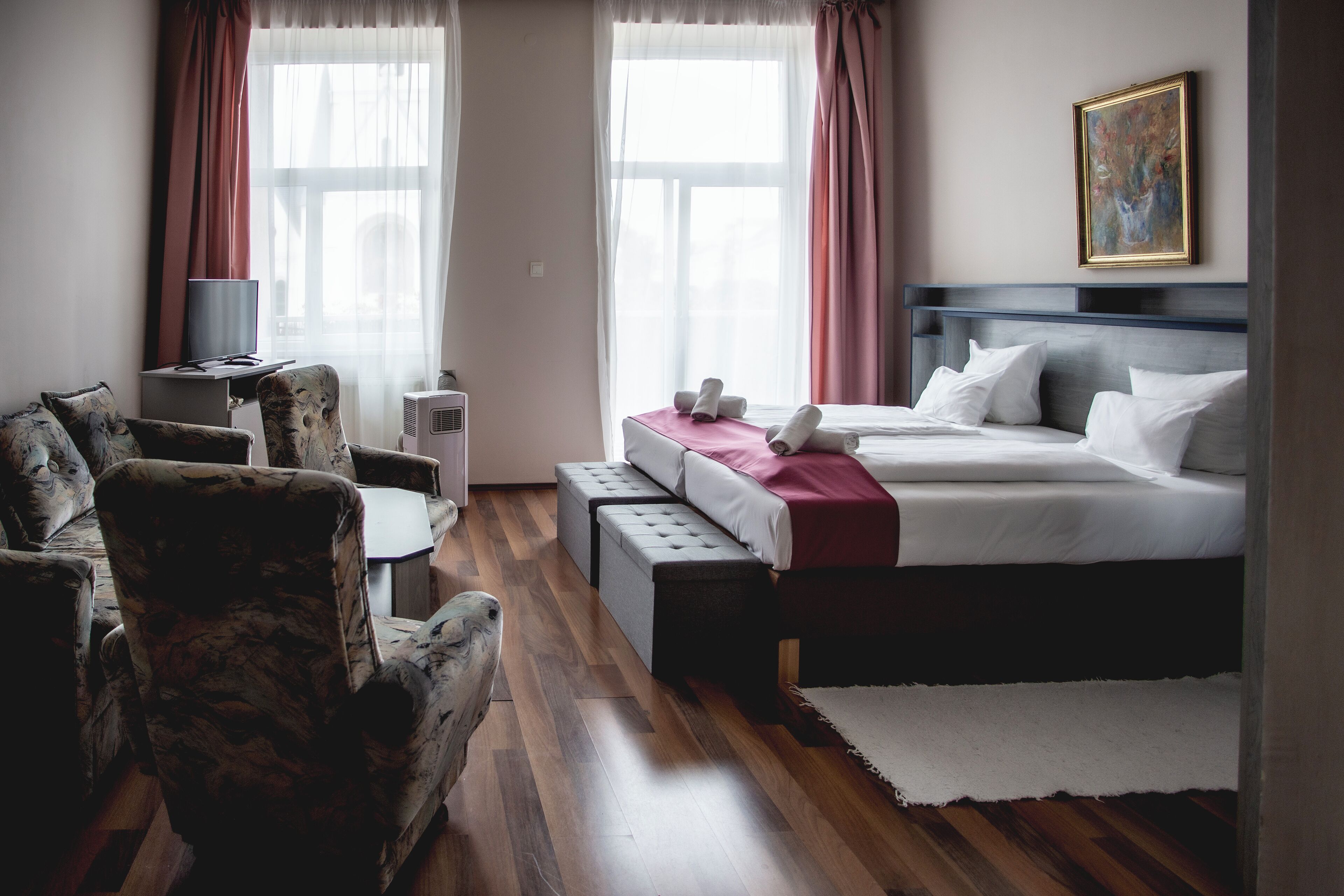 Una habitación de hotel con una cama, dos sillas, una mesita y un ventanal con cortinas.