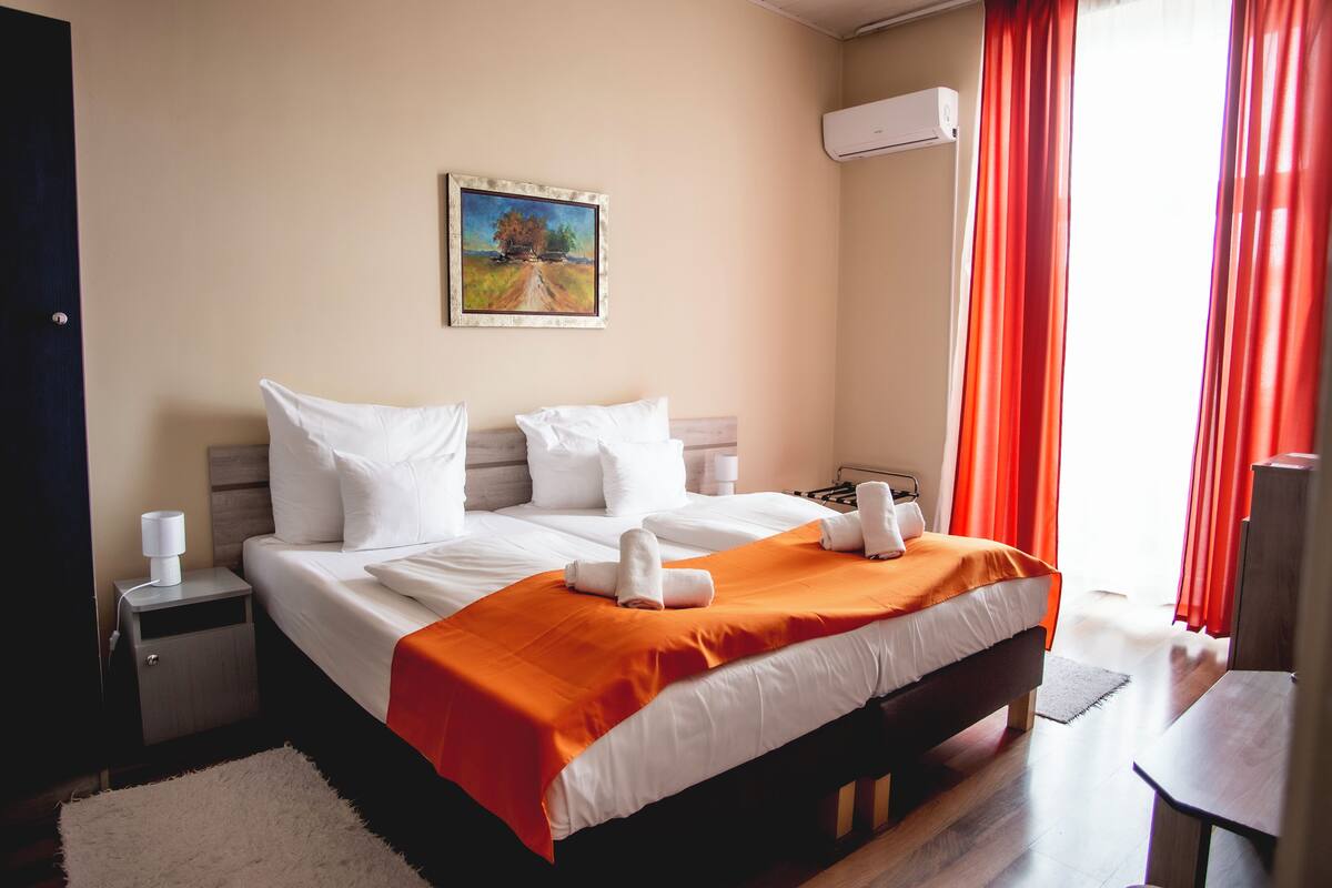 Ein Hotelzimmer mit Bett, Nachttisch, einem Gemälde an der Wand und einer Klimaanlage.