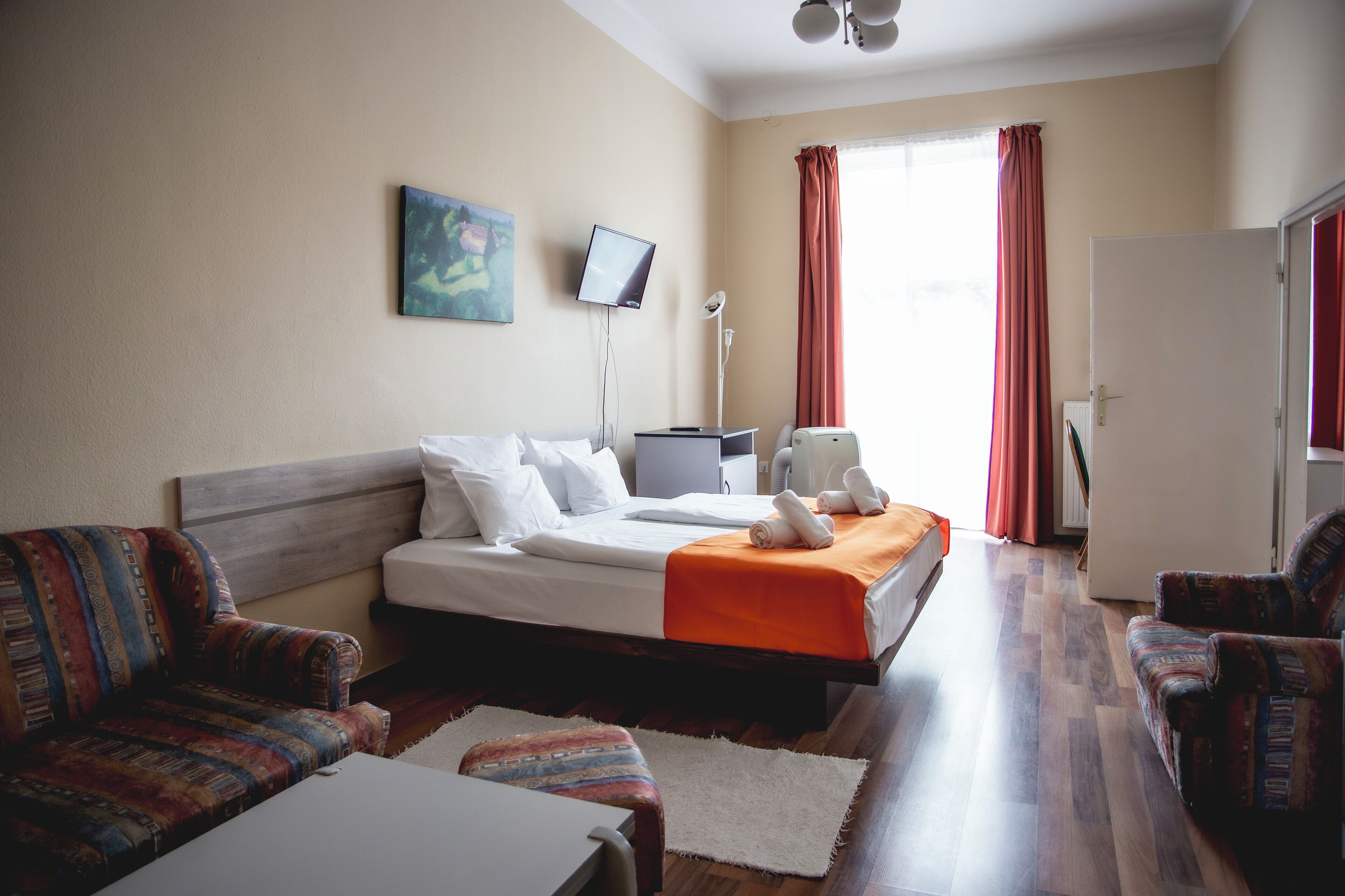 A hotel room with a bed, two armchairs, a desk, a TV, and a window with curtains.