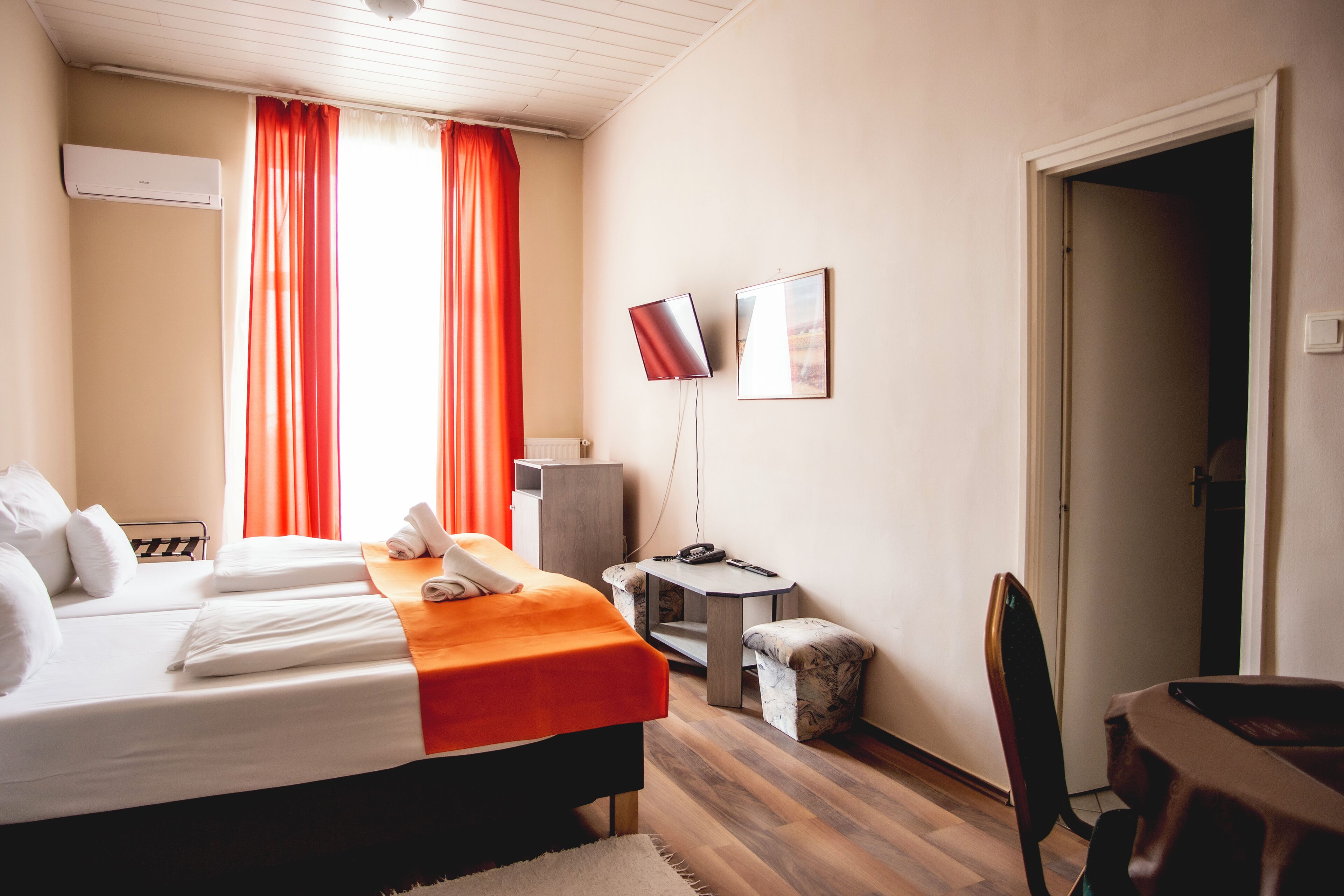 A hotel room with two beds, a desk, a chair, a small table, and a TV.