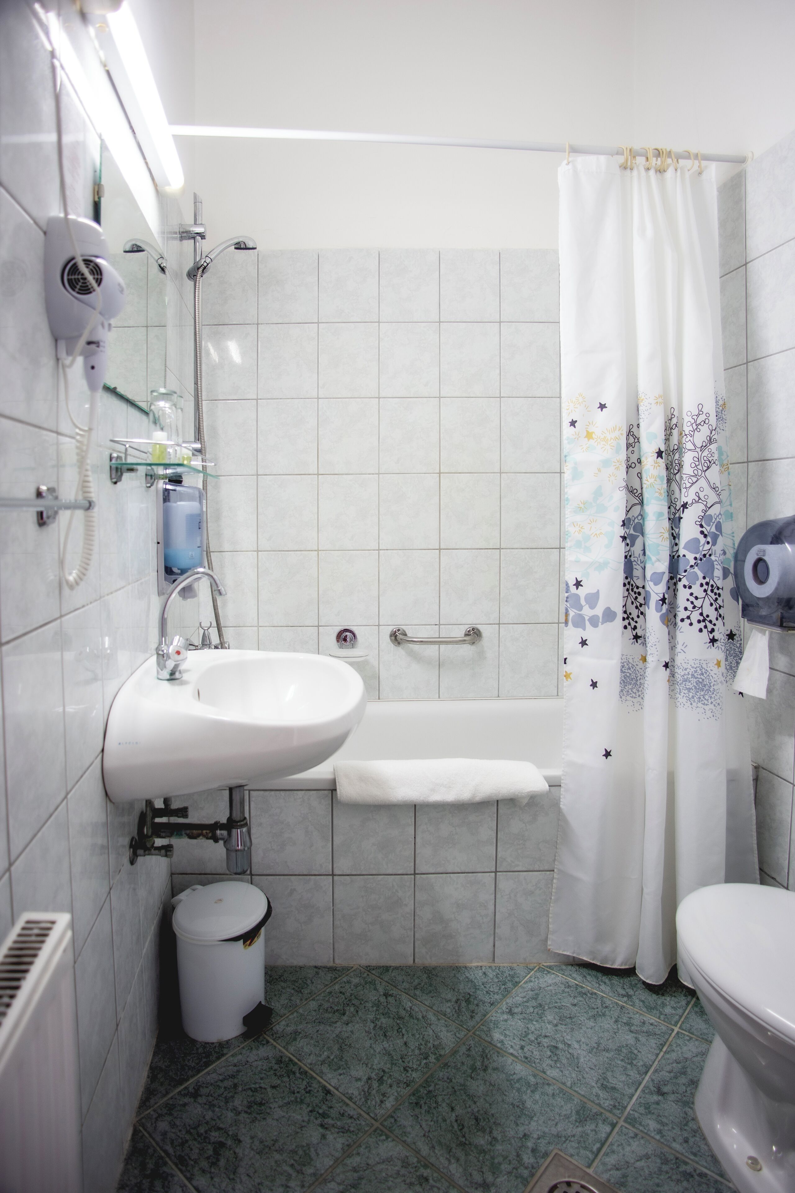 Une salle de bain avec un lavabo blanc, une baignoire et une douche. On y trouve une poubelle blanche et un porte-serviettes.