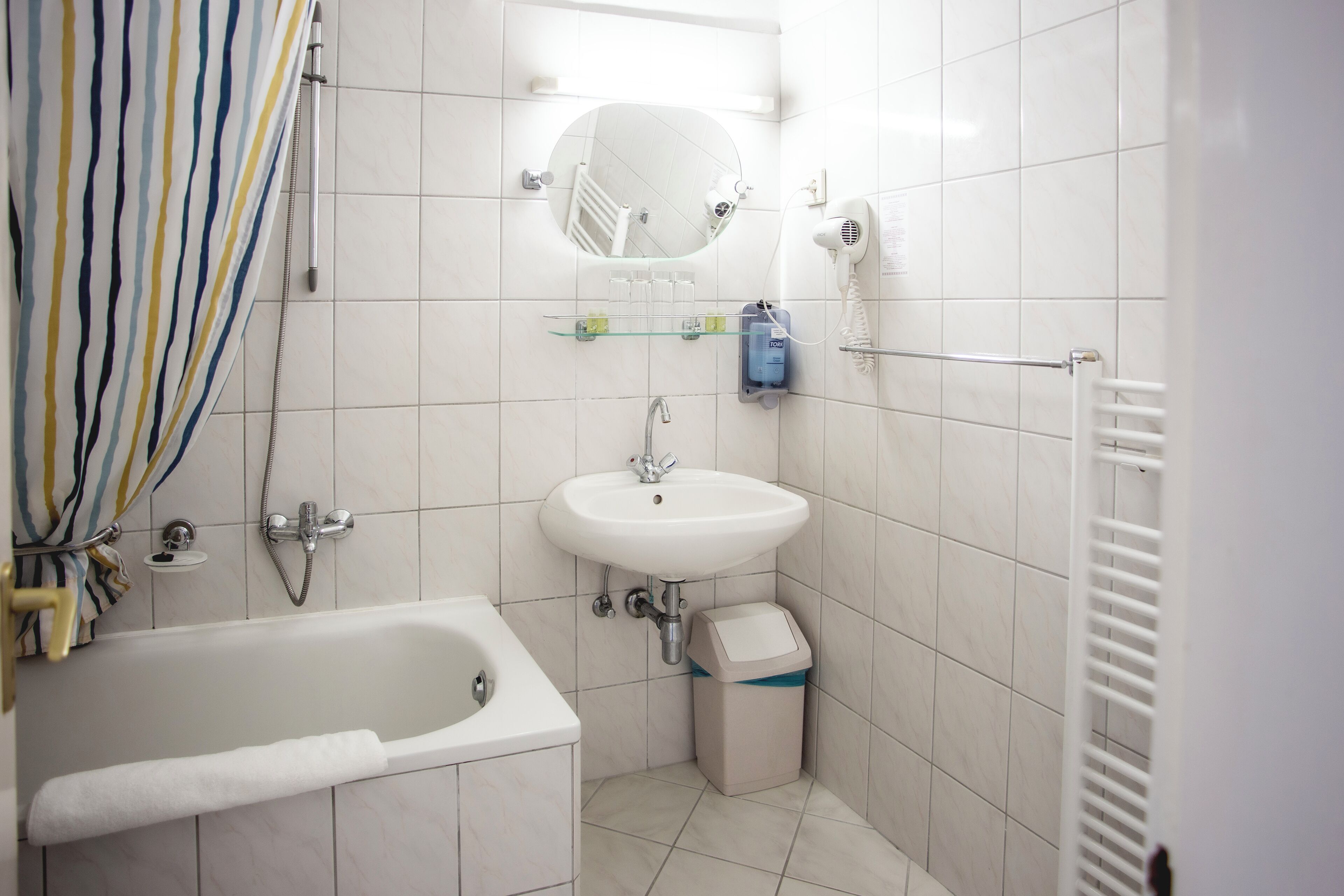 A bathroom with a bathtub, a sink, a mirror, a towel rack, and a trash bin.