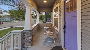 A porch with a stone column, a purple door, and a wicker chair.