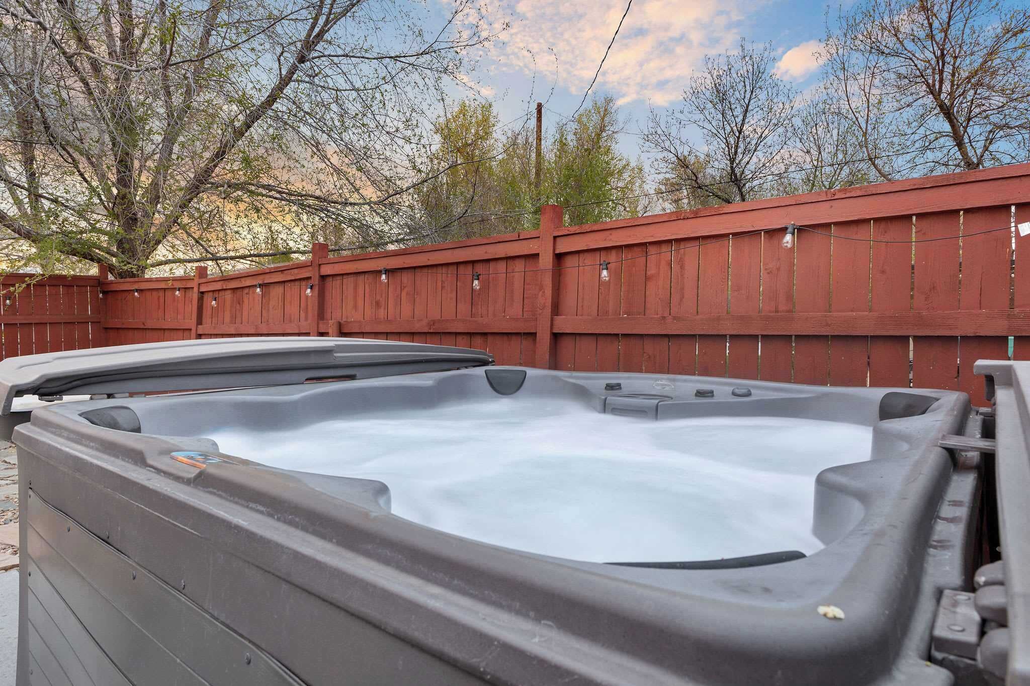 A hot tub in an outdoor setting with a wooden fence and trees in the background.