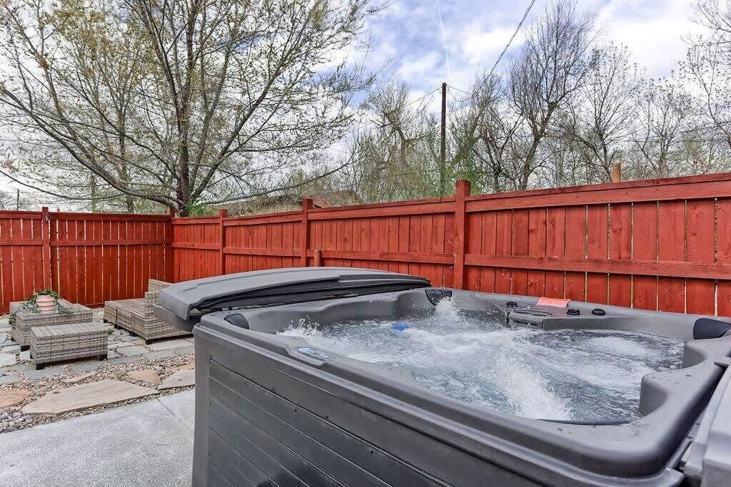 A hot tub in a backyard with a red wooden fence and stone tiles.