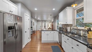 A modern kitchen with white cabinets, stainless steel appliances, and a wooden floor.