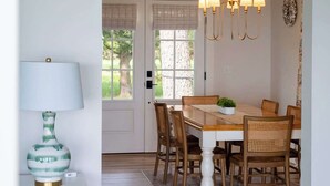 A dining area with a wooden table, wicker chairs, a white lamp, and a chandelier. - Waterfront Tilghman Retreat with Dock, Fire Pit & Sunsets (Tilghman Island)