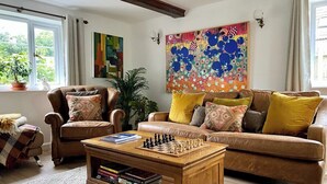 A cozy living room with a brown leather sofa, a wooden coffee table with chess pieces, a dog, and a colorful abstract painting on the wall. - Kings Cottage - Heart of the Deverills (Warminster)
