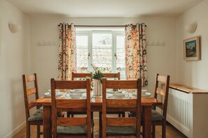 Comedor con mesa dispuesta para cuatro, sillas de madera, ventana con cortinas y un radiador en la pared.