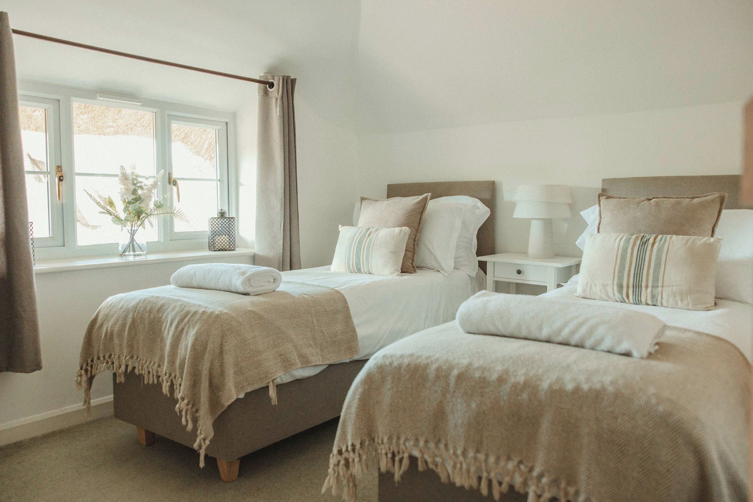 Une chambre avec deux lits, une fenêtre avec des rideaux, une table de chevet avec une lampe et un vase rempli de fleurs.
