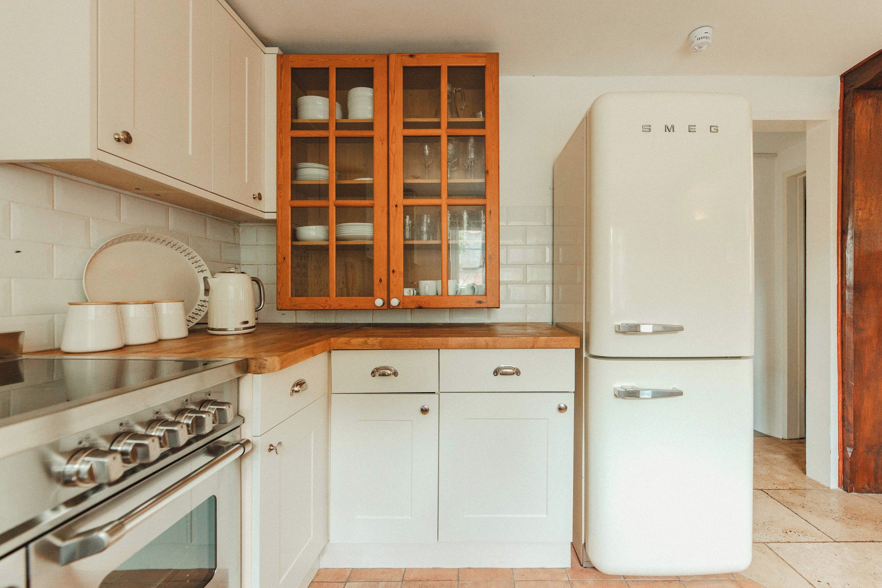 Une cuisine avec des meubles blancs, un plan de travail en bois, un réfrigérateur blanc et une cuisinière.