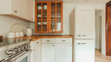 Une cuisine avec des meubles blancs, un plan de travail en bois, un réfrigérateur blanc et une cuisinière.