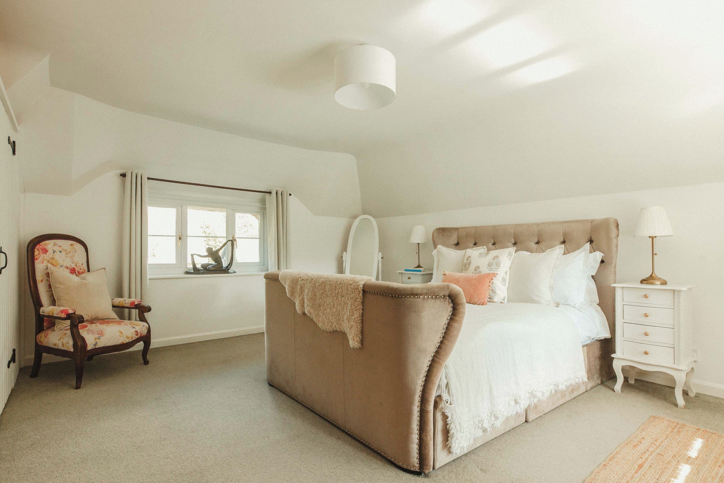 A bedroom with a large bed, a chair, a bedside table, and a window.