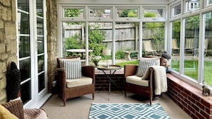 A sunroom with wicker furniture, a small table, and a view of a backyard. - Kings Cottage - Heart of the Deverills (Warminster)