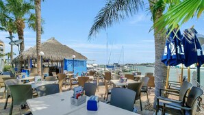 An outdoor dining area with tables and chairs, a thatched-roof structure, and a view of the sea. - Waterfront Condo in Anglers Cove With Pools and Spas (Marco Island)